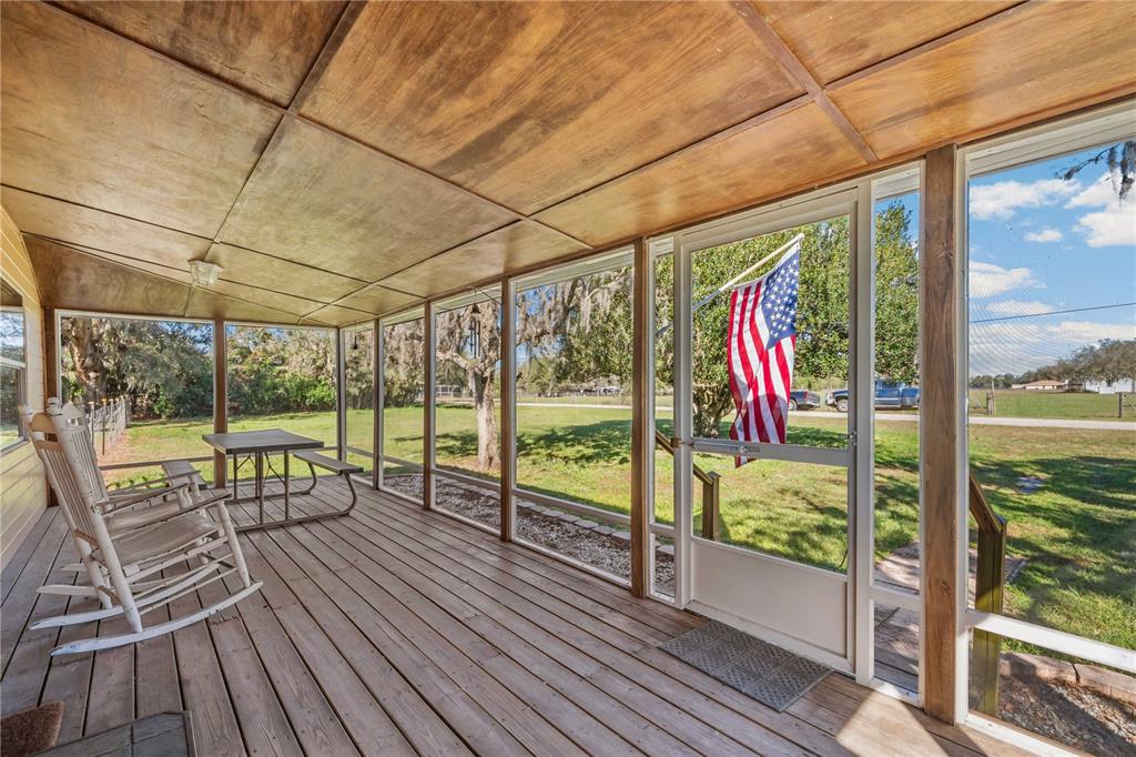 A screened-in wooden porch features rocking chairs, a picnic table, and an American flag — 2615 CR 762, WEBSTER, FL
