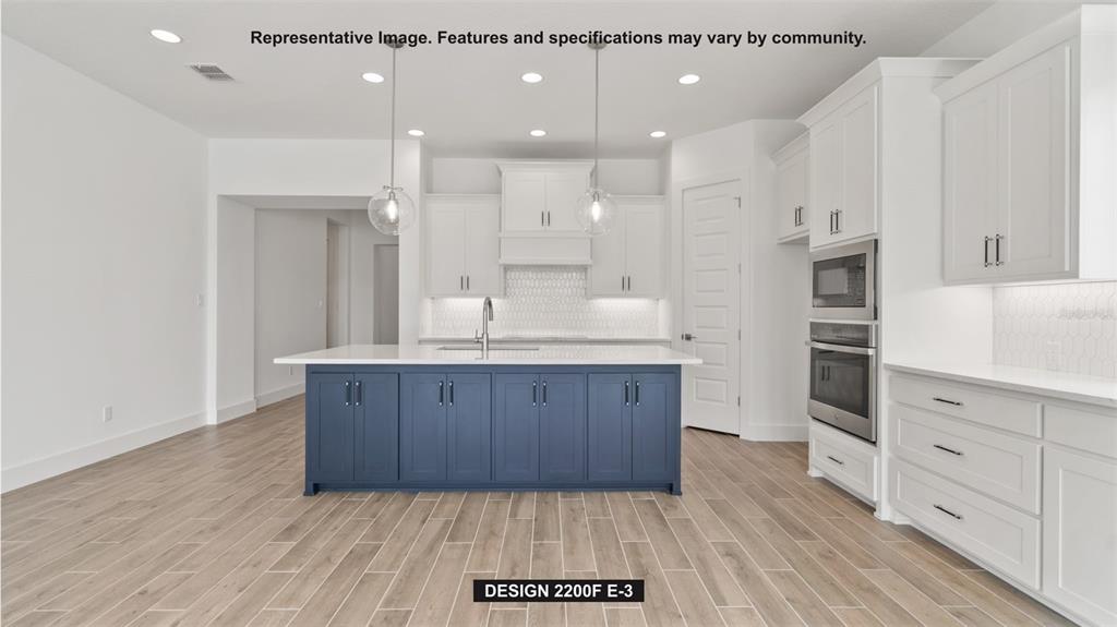 This kitchen features white cabinetry, a blue island, stainless steel appliances, and wood-look tile flooring — 326 HOLLY BANK AVENUE, NOKOMIS, FL
