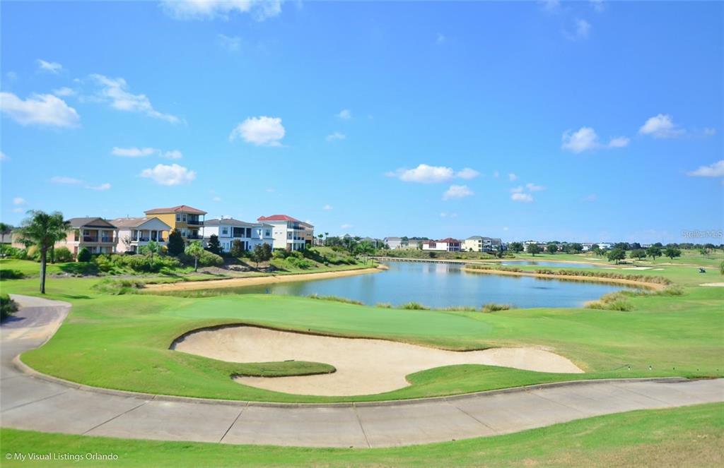A golf course green and sand bunker overlook a lake with houses in the background — 7622 EXCITEMENT DRIVE, REUNION, FL