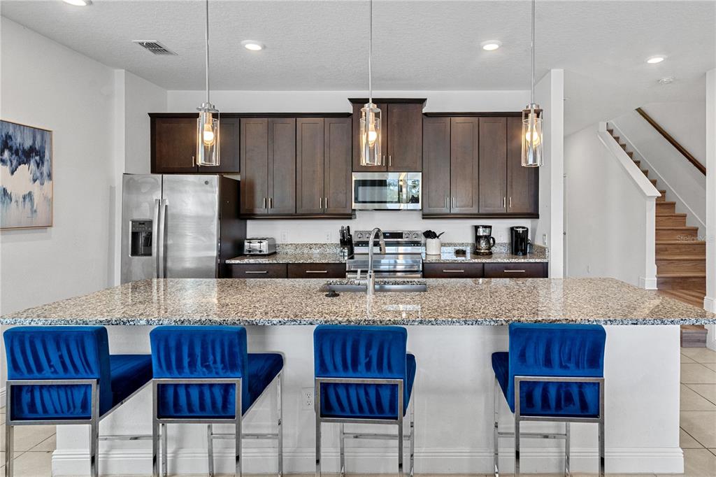A kitchen features dark wood cabinets, granite countertops, a large island, and four blue stools — 7622 EXCITEMENT DRIVE, REUNION, FL