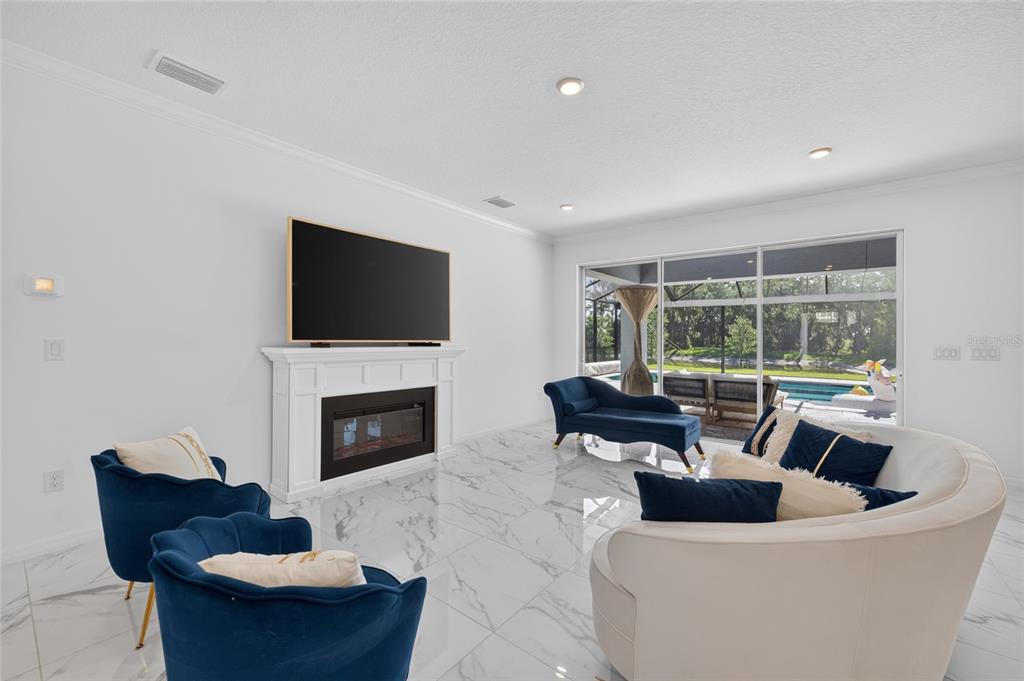 A living room features white marble floors, a fireplace with a television, and blue furniture — 33751 LANDSMAN LOOP, WESLEY CHAPEL, FL