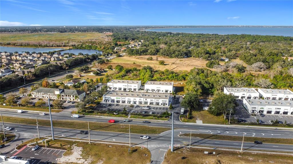 An aerial view shows commercial buildings, a parking lot, and a road near a lake — 1370 S NARCOOSSEE ROAD, ST CLOUD, FL