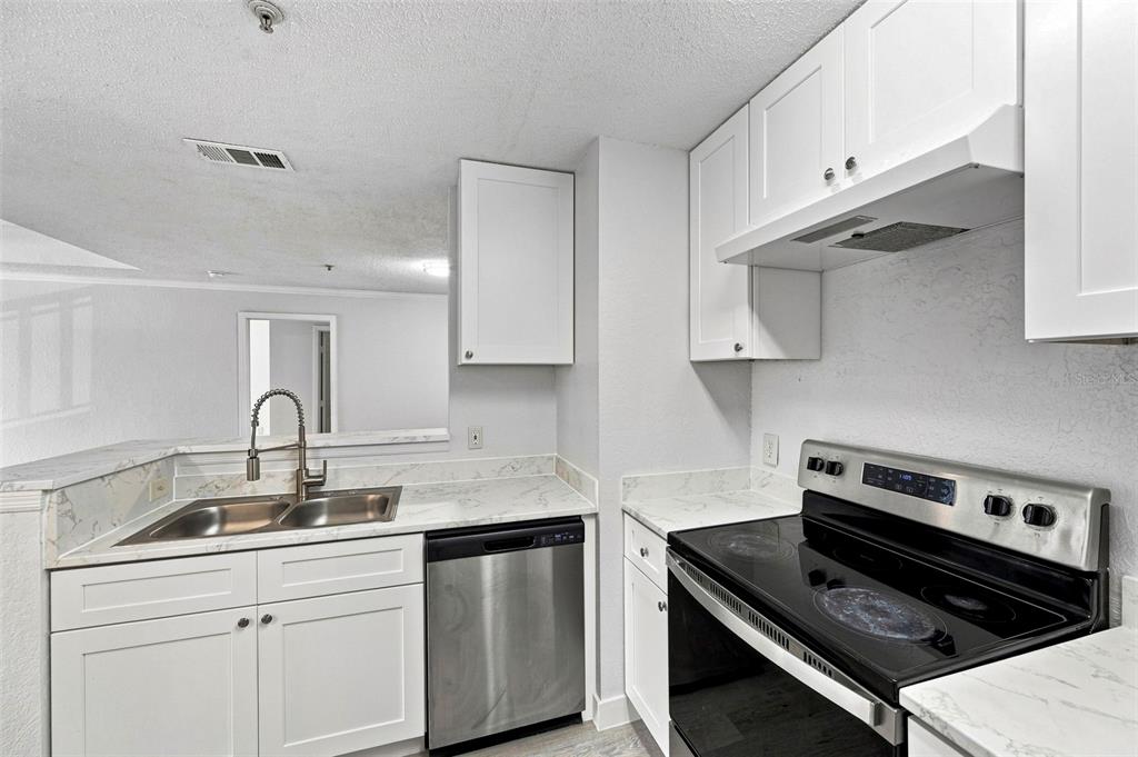 A kitchen features white cabinetry, marble-look countertops, stainless steel appliances, and light wood-look flooring — 18001 RICHMOND PLACE DRIVE UNIT 136, TAMPA, FL
