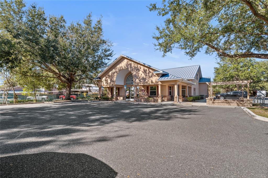 A tan commercial building with a metal roof stands behind a large asphalt parking lot — 3300 N HIGHWAY 19A, MOUNT DORA, FL