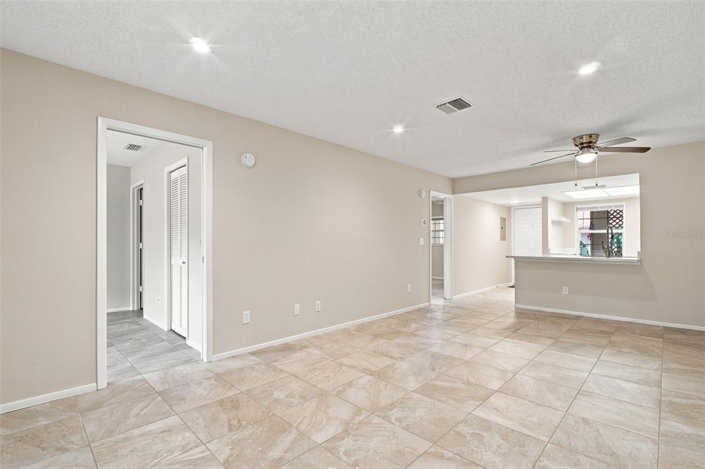 A living area with light-colored tile flooring, beige walls, and an open kitchen pass-through — 2460 NORTHSIDE DRIVE UNIT 1202, CLEARWATER, FL