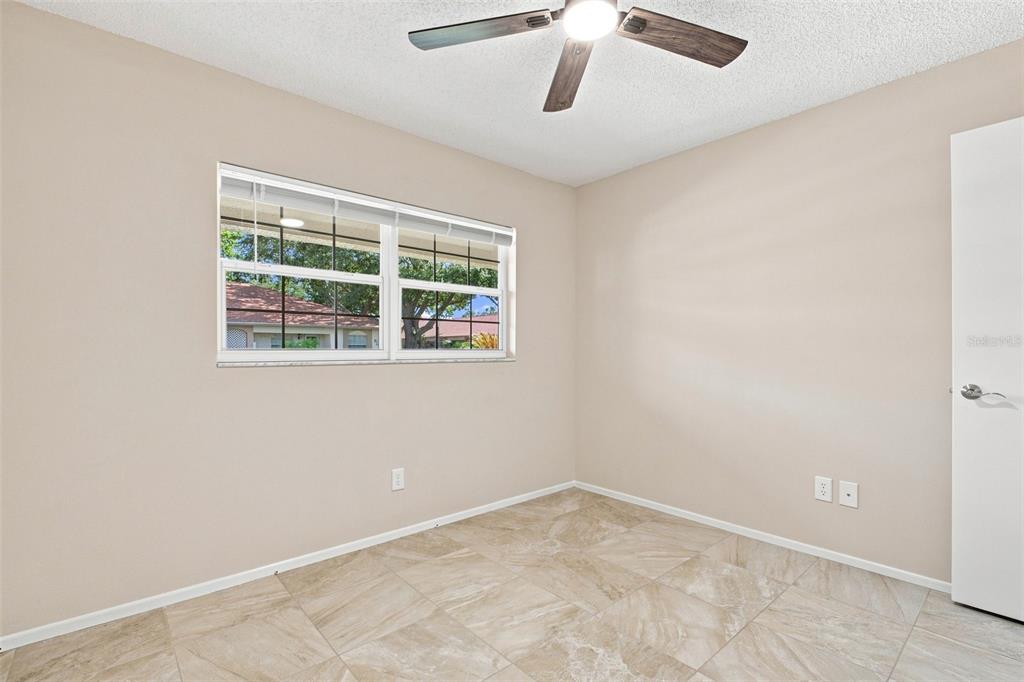 A bedroom with beige walls, tile flooring, a ceiling fan, and a window — 2460 NORTHSIDE DRIVE UNIT 1202, CLEARWATER, FL