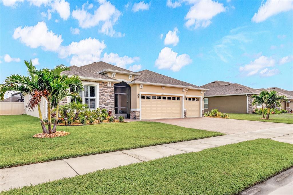 A single-story house with a stone facade, beige garage doors, and a palm tree — 6691 CAMEO DRIVE, GRANT, FL