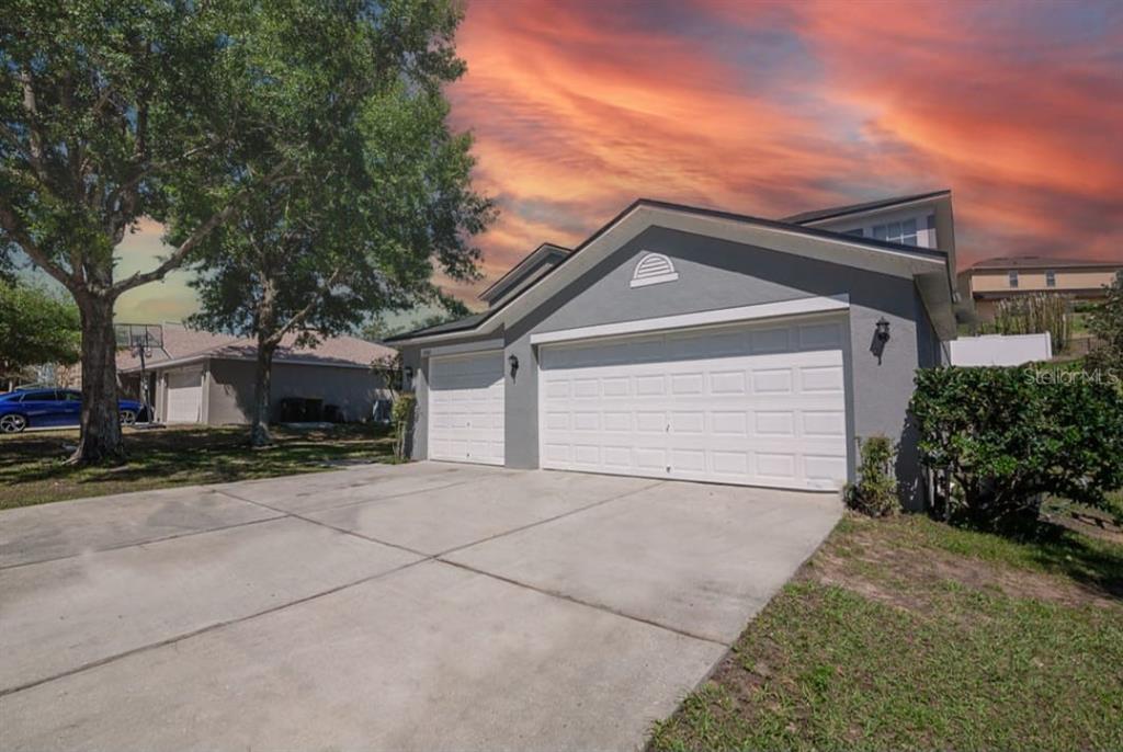 A gray house with a three-car garage and a concrete driveway under a sunset sky — 1846 WAKE FOREST AVENUE, CLERMONT, FL