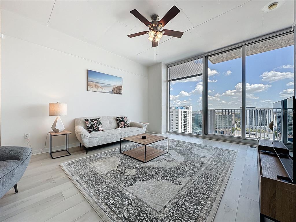 A living room features a sofa, coffee table, television, and floor-to-ceiling windows overlooking a city — 155 S COURT AVENUE UNIT 1911, ORLANDO, FL