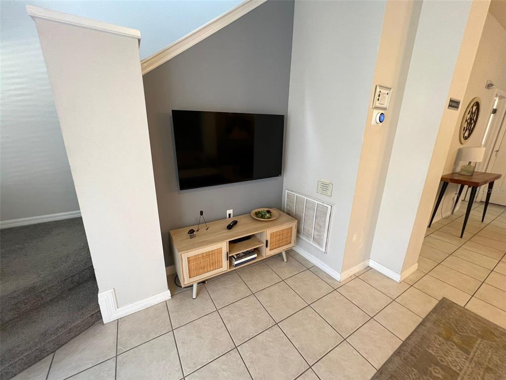A wall-mounted television sits above a light wood media console in a tiled room — 8563 BAY LILLY LOOP, KISSIMMEE, FL