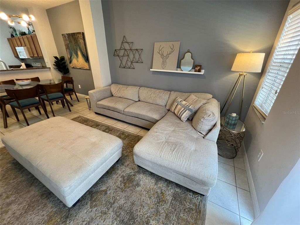 A living room features a beige sectional sofa, a large ottoman, and a wall shelf — 8563 BAY LILLY LOOP, KISSIMMEE, FL