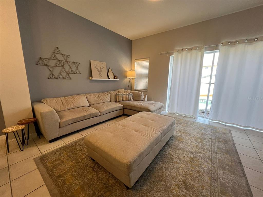 A living room features a beige sectional sofa, a matching ottoman, and a patterned rug — 8563 BAY LILLY LOOP, KISSIMMEE, FL