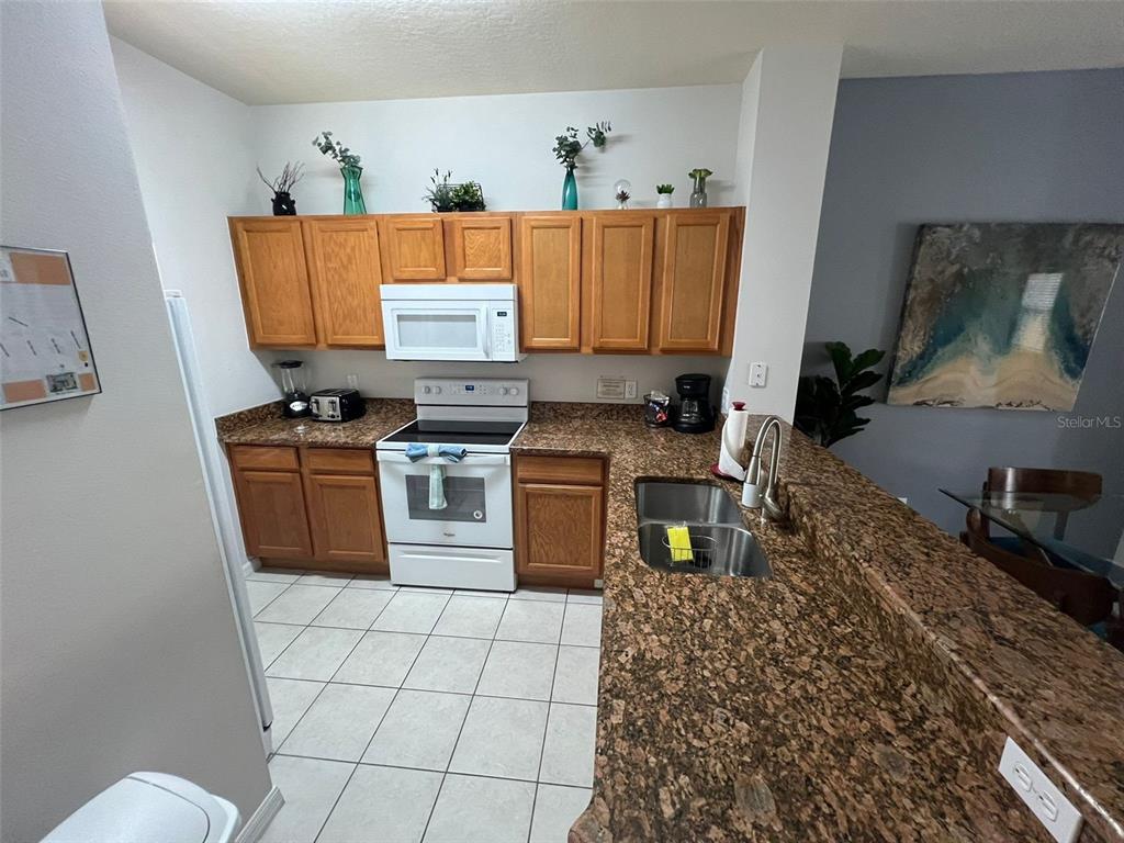 A kitchen features oak cabinets, granite countertops, white appliances, and a tiled floor — 8563 BAY LILLY LOOP, KISSIMMEE, FL