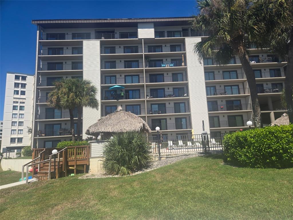 A multi-story apartment building with balconies overlooks a swimming pool and a thatched umbrella — 650 ISLAND WAY UNIT 202, CLEARWATER BEACH, FL