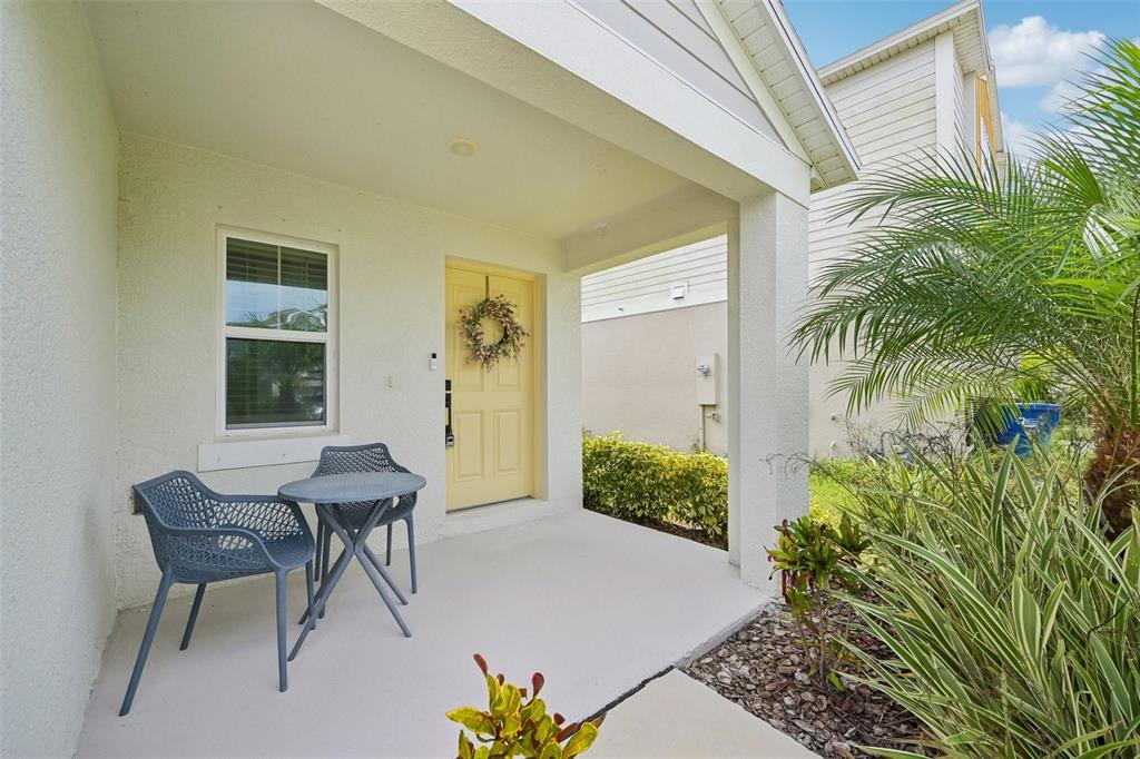 A covered front porch features a yellow door, two grey chairs, and a small table — 7728 TWINLEAF TERRACE, PARRISH, FL