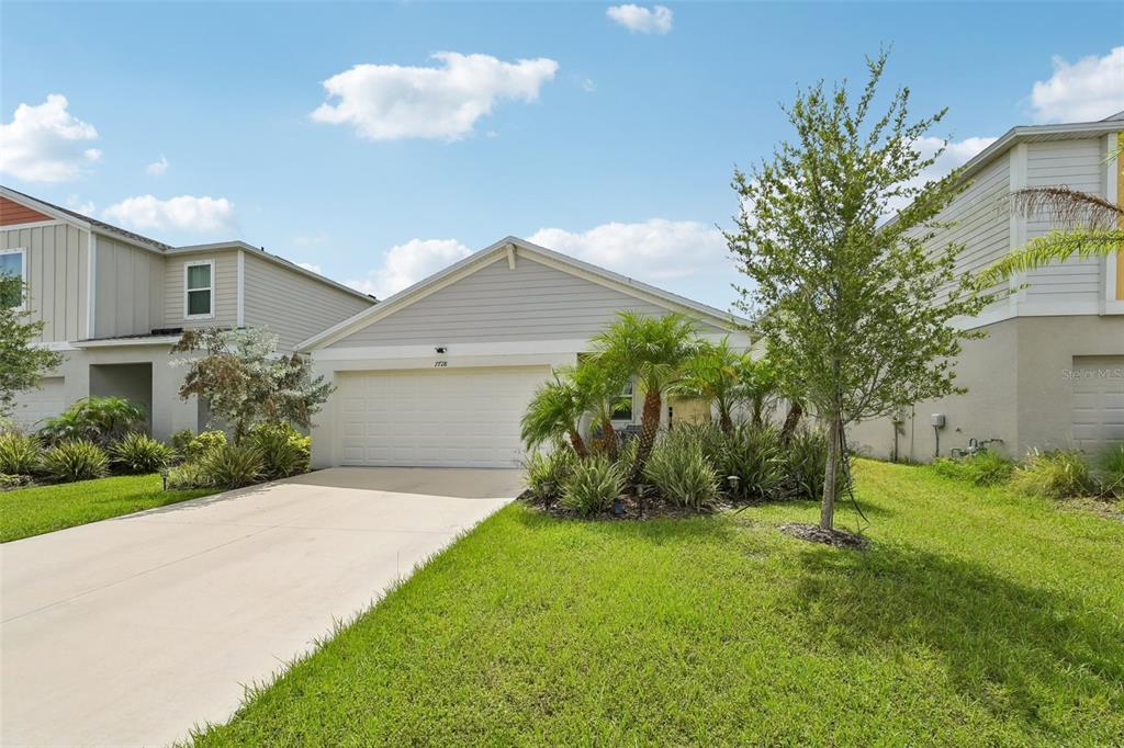A single-story suburban house with a beige exterior, a two-car garage, and a front lawn — 7728 TWINLEAF TERRACE, PARRISH, FL