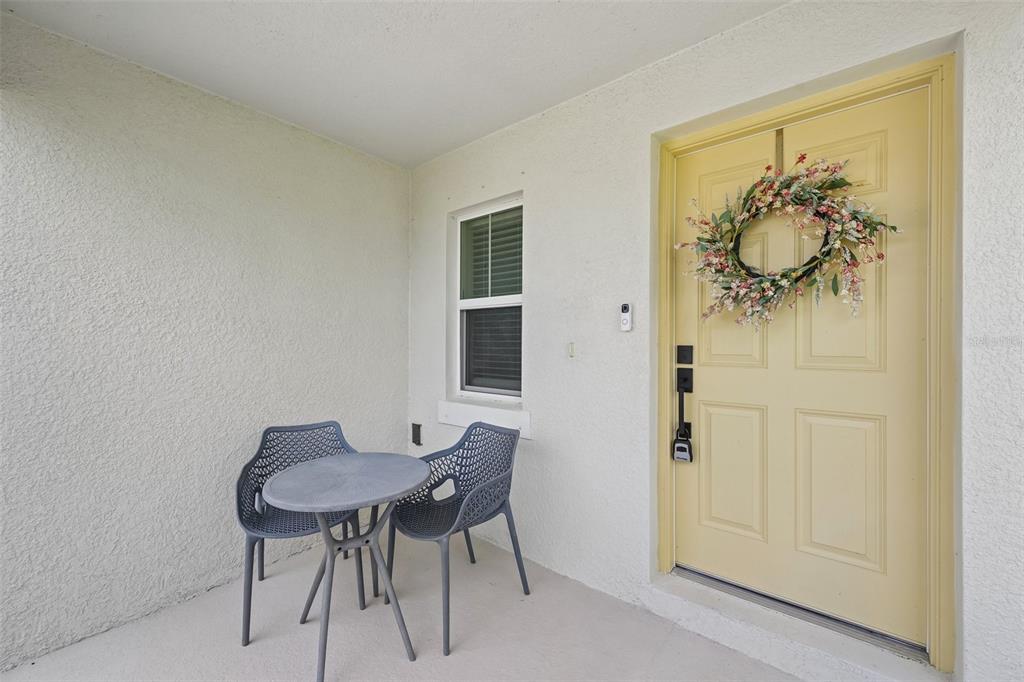 A small covered porch features a bistro set, a window, and a yellow front door — 7728 TWINLEAF TERRACE, PARRISH, FL