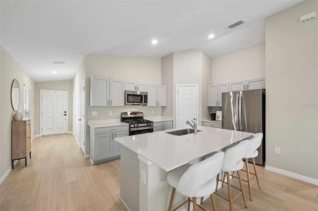 A modern kitchen features light gray cabinetry, stainless steel appliances, and a white quartz island — 7728 TWINLEAF TERRACE, PARRISH, FL