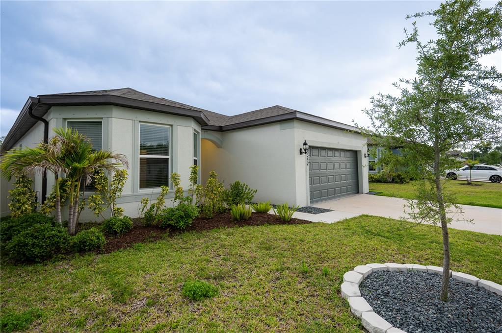 A single-story house with a beige stucco exterior, a gray garage door, and front landscaping — 3022 61ST TERRACE E, ELLENTON, FL