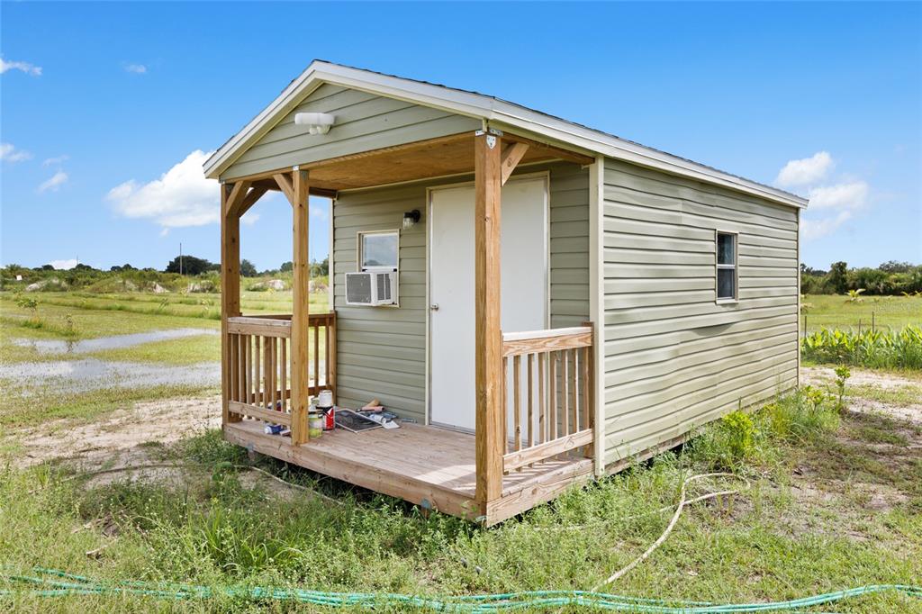 A small, light green shed with a front porch sits in a grassy, open field — 20914 NW 280TH STREET, OKEECHOBEE, FL
