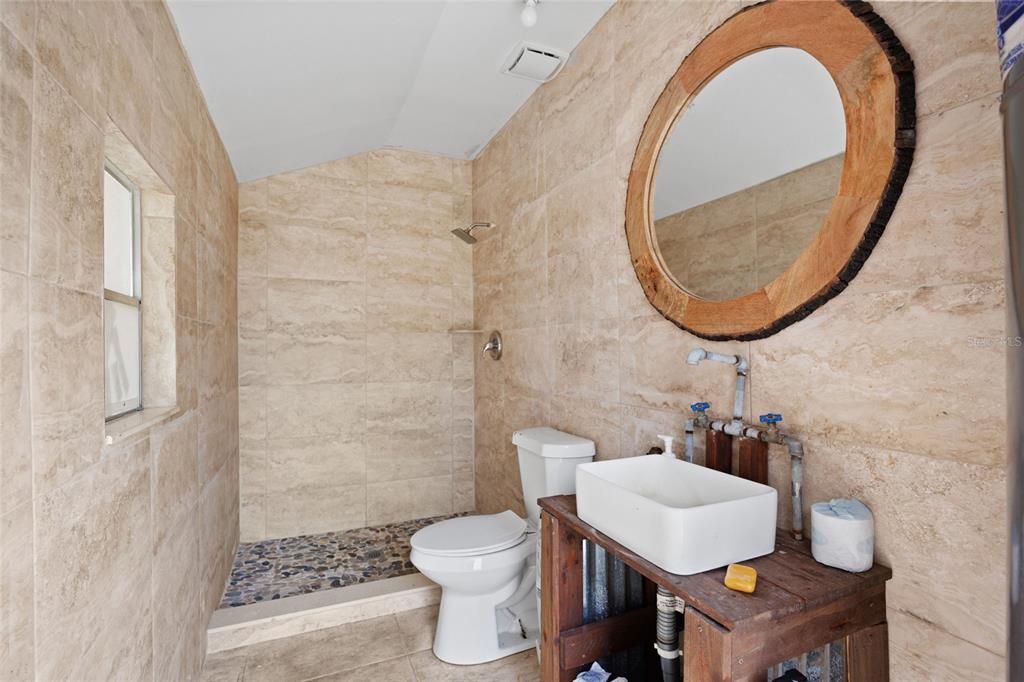 A bathroom features beige tiled walls, a walk-in shower, a toilet, and a rustic wood vanity — 20914 NW 280TH STREET, OKEECHOBEE, FL