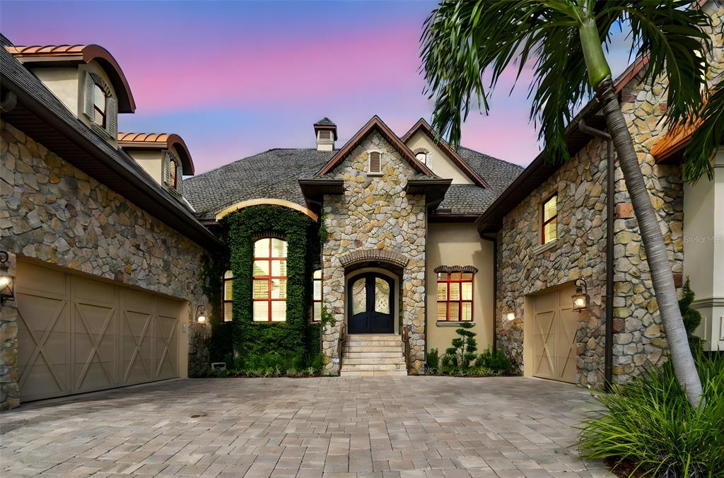 A stone-clad house with a paved driveway, two garages, and a central arched entryway — 5405 LEILANI DRIVE, ST PETE BEACH, FL