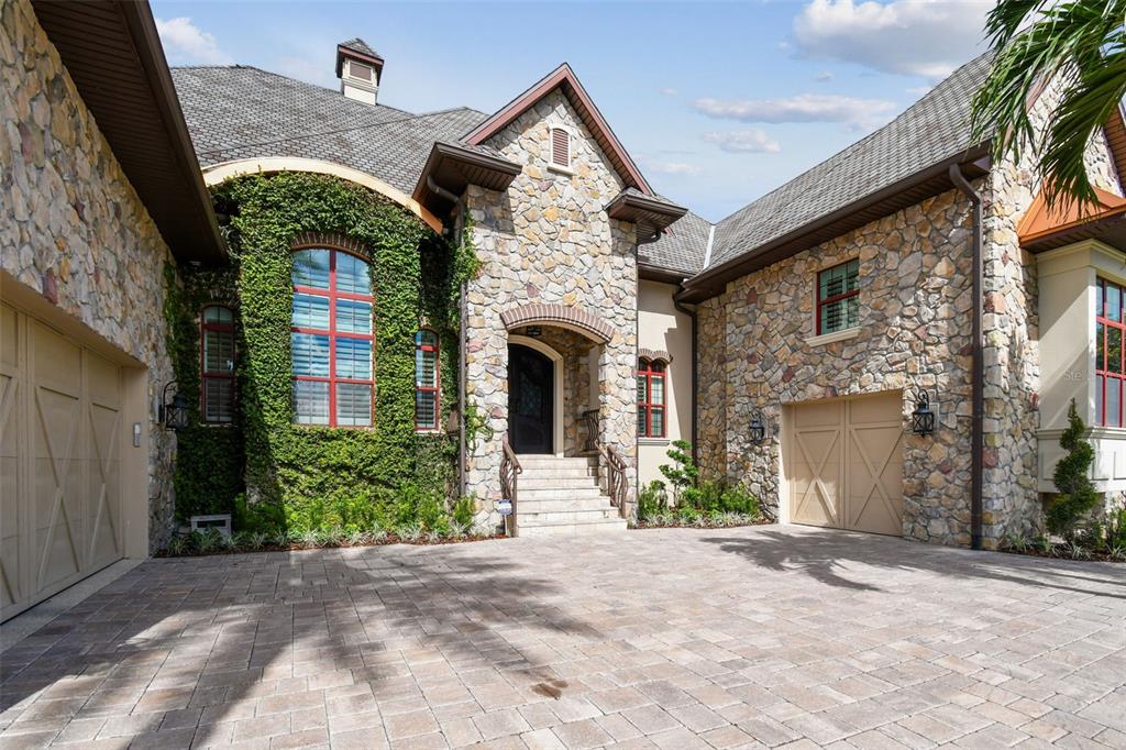 A stone-clad house with two garages, a central arched entryway, and ivy-covered walls — 5405 LEILANI DRIVE, ST PETE BEACH, FL