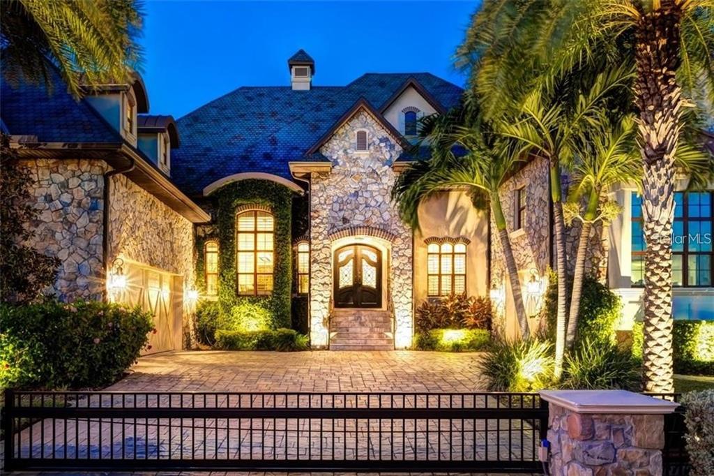 A stone-clad luxury house with a paved driveway and gated entrance at twilight — 5405 LEILANI DRIVE, ST PETE BEACH, FL