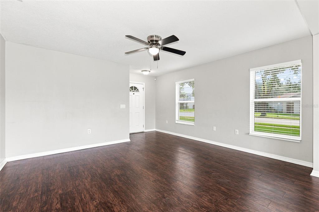 An empty room with dark wood flooring, light gray walls, a ceiling fan, and windows — 11773 MANGO CROSS COURT, SEFFNER, FL