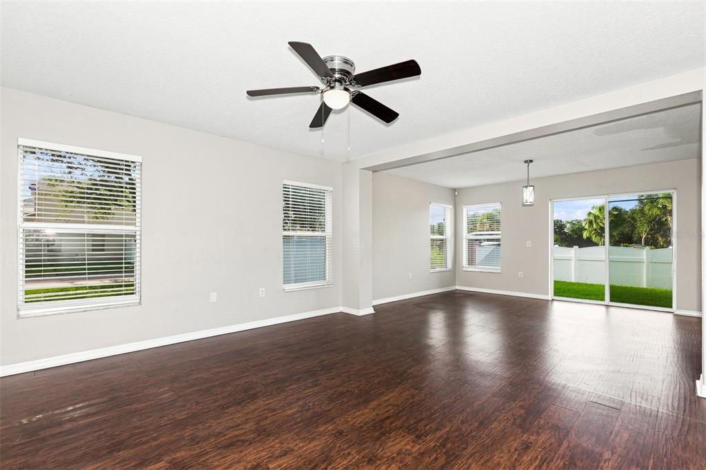An empty living room features dark wood-look flooring, a ceiling fan, and sliding glass doors — 11773 MANGO CROSS COURT, SEFFNER, FL