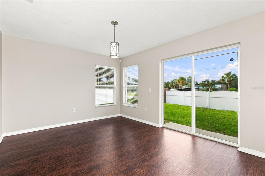 A dining area with dark wood flooring, two windows, a pendant light, and sliding glass doors — 11773 MANGO CROSS COURT, SEFFNER, FL