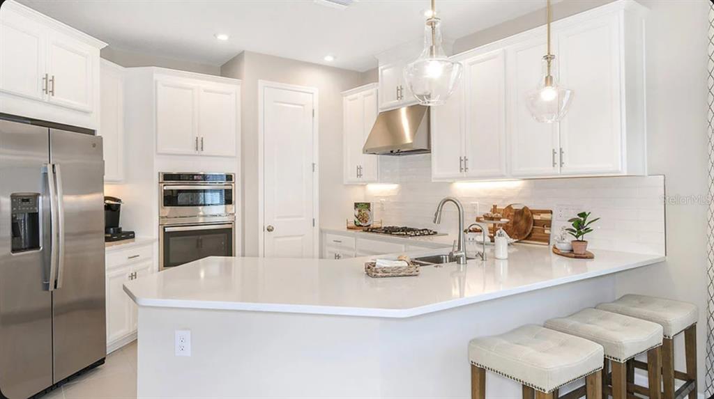 A modern kitchen features white cabinets, stainless steel appliances, and a white quartz breakfast bar — 32477 SEA LOCH LOOP, MOUNT DORA, FL