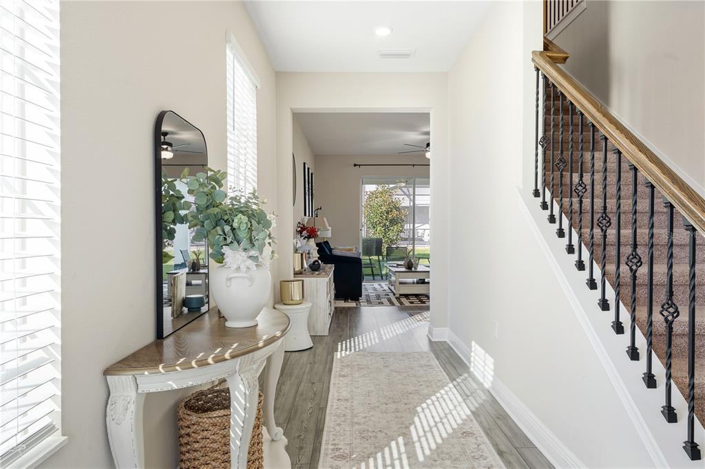 A bright entryway features a wood-topped console table, a staircase with iron railings, and wood-look flooring — 7853 SOMERSWORTH DRIVE, KISSIMMEE, FL