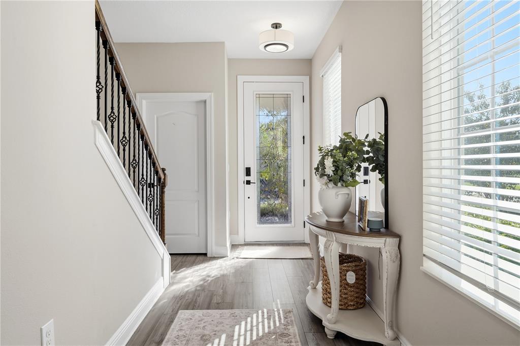 A bright entryway features a staircase with iron railings, a console table, and a front door — 7853 SOMERSWORTH DRIVE, KISSIMMEE, FL