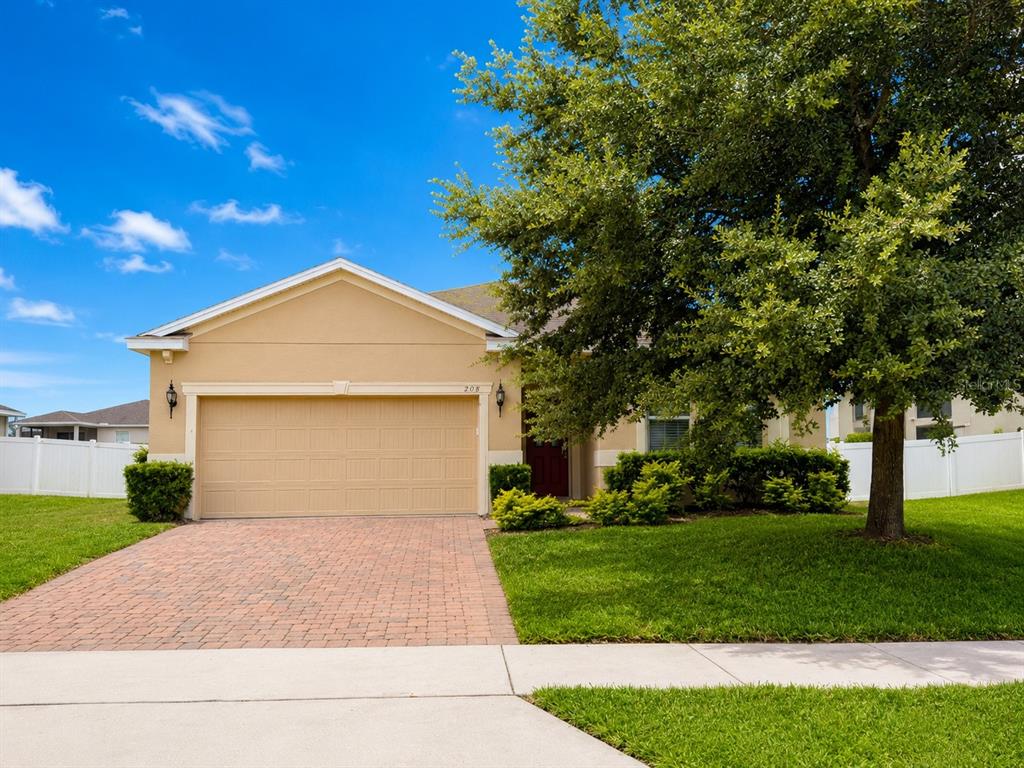 A tan single-story house with a brick driveway and a large tree in the front yard — 908 GLAZEBROOK LOOP, ORANGE CITY, FL