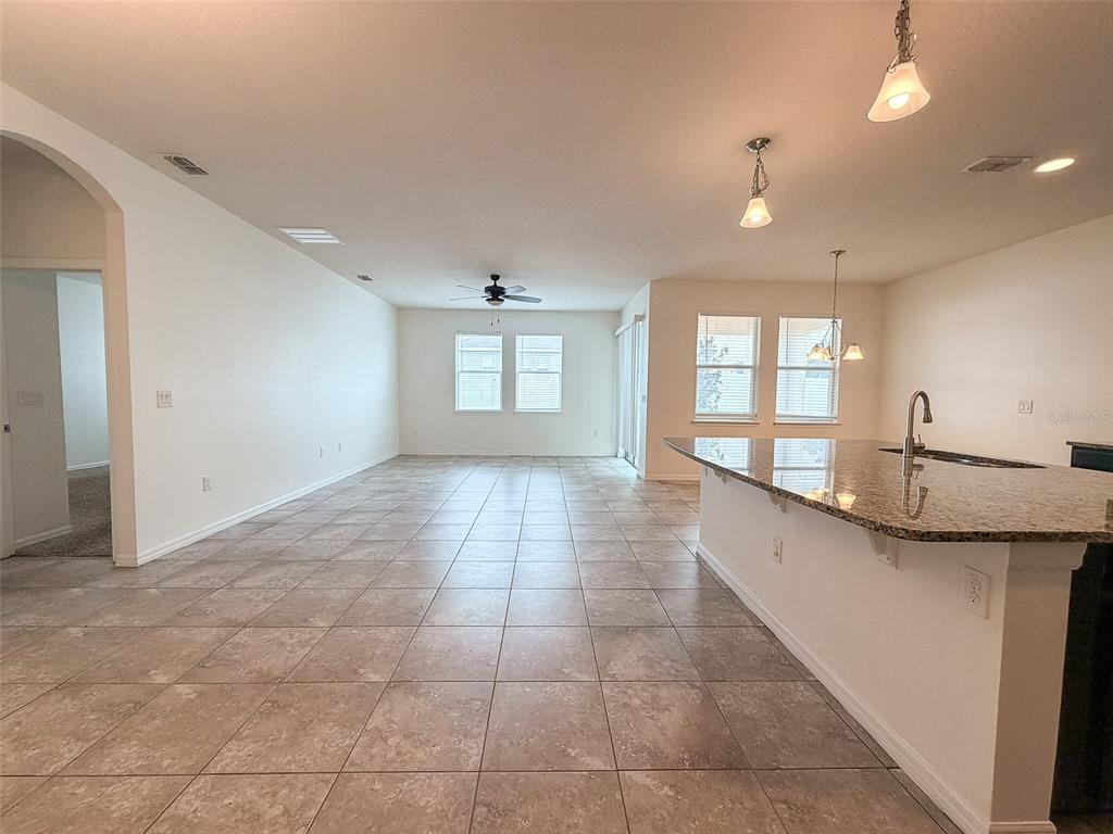 An open-concept kitchen and living area featuring tile flooring, granite countertops, and recessed lighting — 908 GLAZEBROOK LOOP, ORANGE CITY, FL