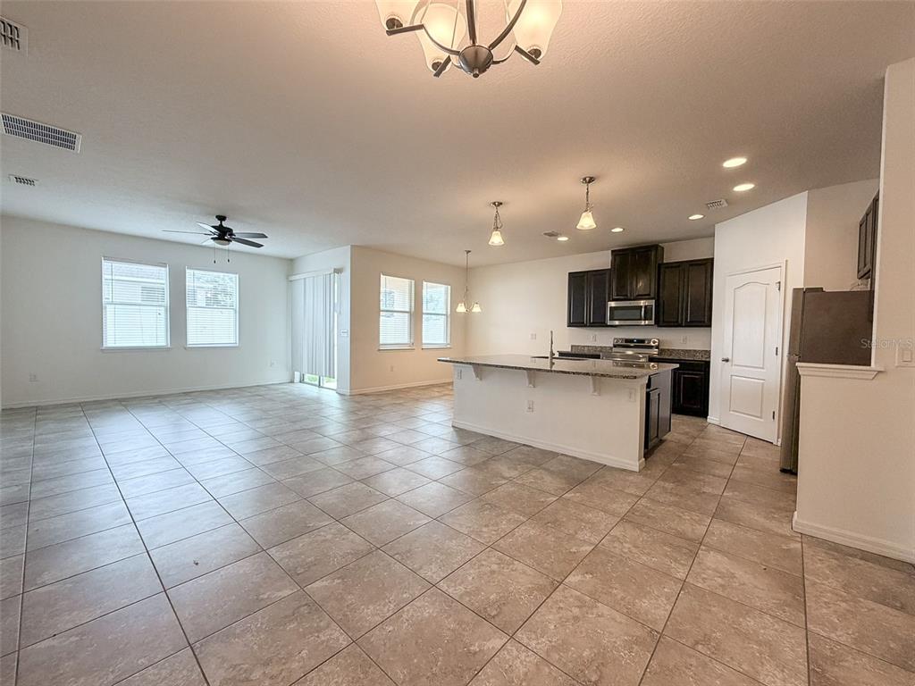An open-concept kitchen and living area features tile flooring, dark cabinetry, and a granite island — 908 GLAZEBROOK LOOP, ORANGE CITY, FL