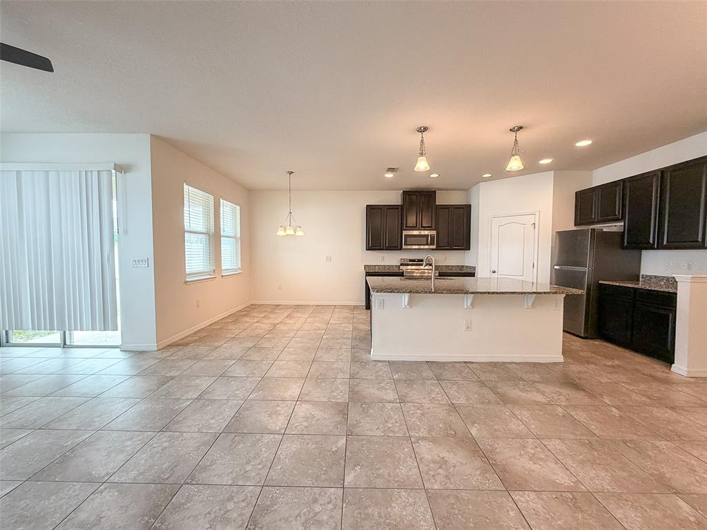 An open-concept kitchen features dark cabinetry, granite countertops, a center island, and tiled flooring — 908 GLAZEBROOK LOOP, ORANGE CITY, FL