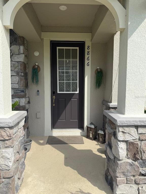 A dark front door with a glass pane is framed by stone pillars and stucco walls — 8866 HERENCIA ALY, WINDERMERE, FL