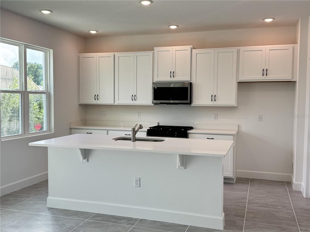 A modern kitchen features white cabinets, a quartz-topped island with a sink, and tile flooring — 4299 LAUREL SITE LOOP, APOPKA, FL