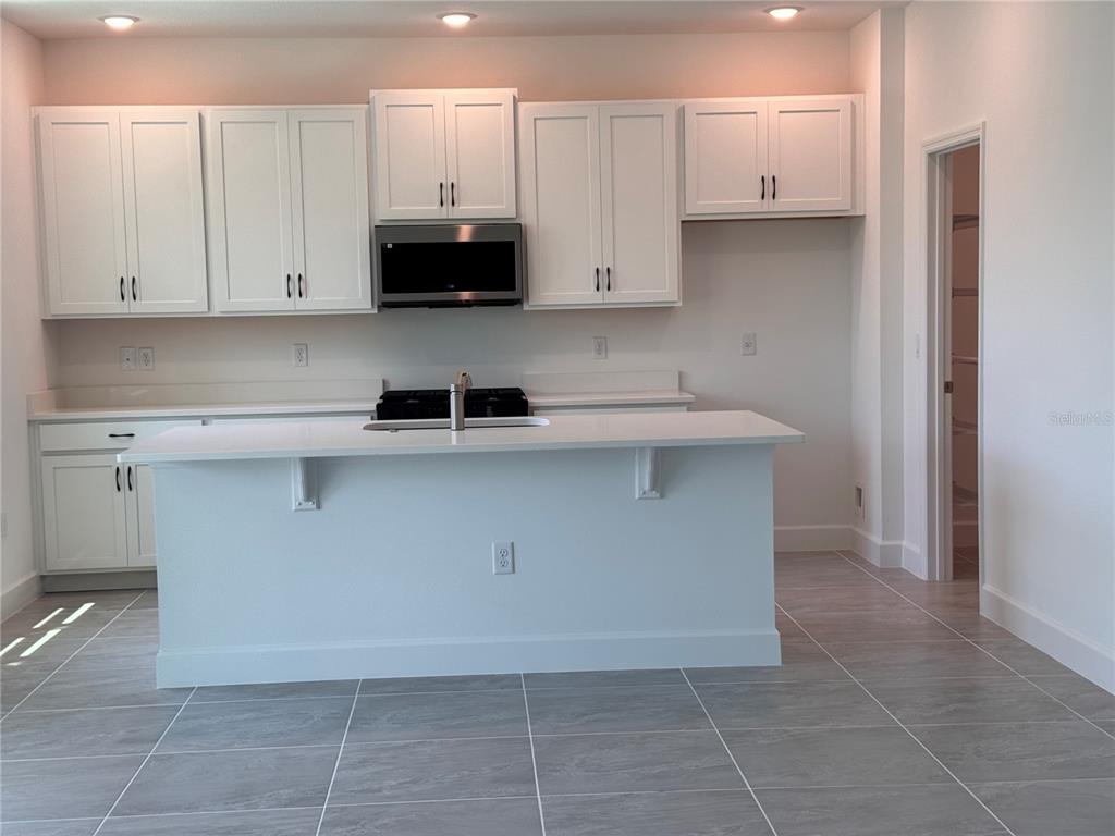 A modern kitchen features white cabinetry, a central island with a sink, and tiled flooring — 4299 LAUREL SITE LOOP, APOPKA, FL