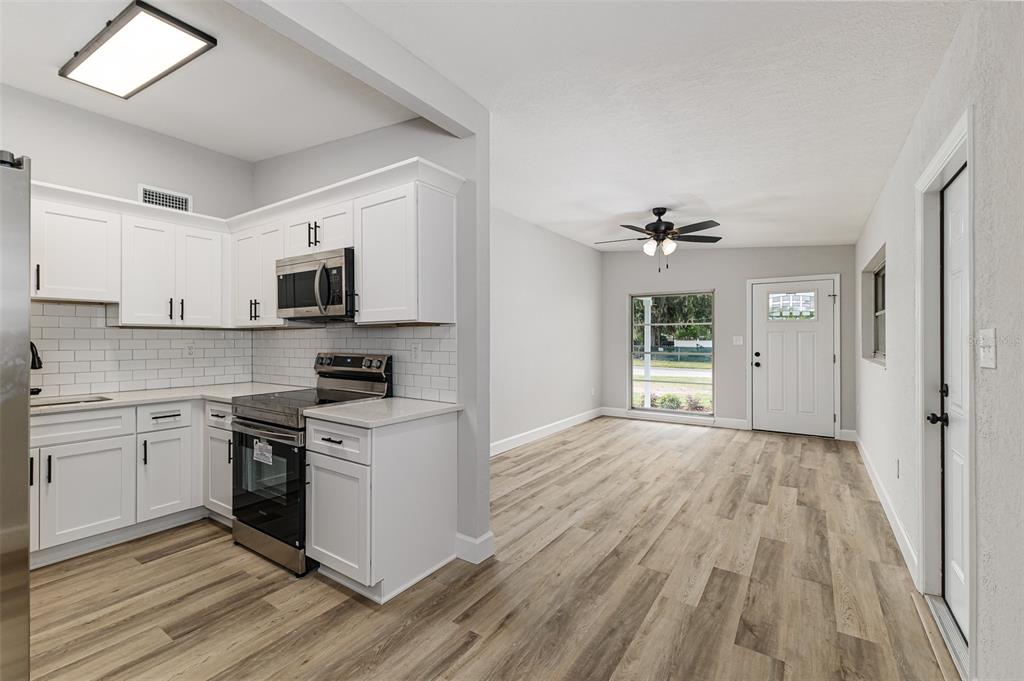 A kitchen with white cabinets and stainless steel appliances opens into a living area with flooring — 465 FORREST DRIVE, BARTOW, FL