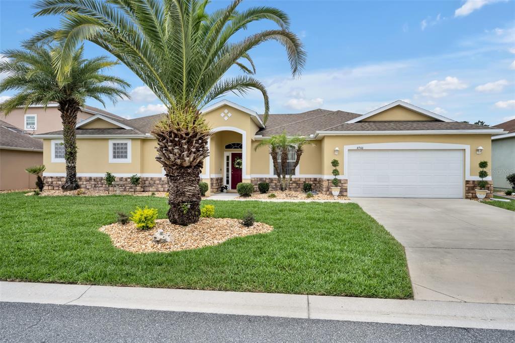 A single-story suburban house with a tan exterior, stone accents, a palm tree, and a garage — 4946 NE 124TH ROAD, OXFORD, FL