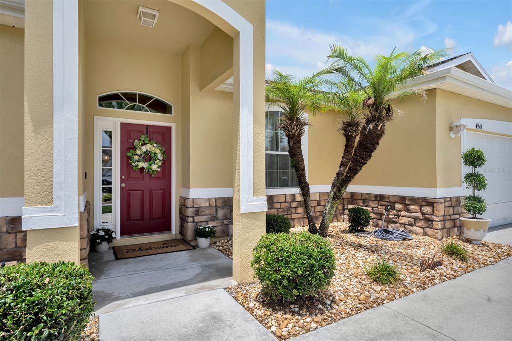 The exterior of a house features a red front door, stone accents, and palm trees — 4946 NE 124TH ROAD, OXFORD, FL