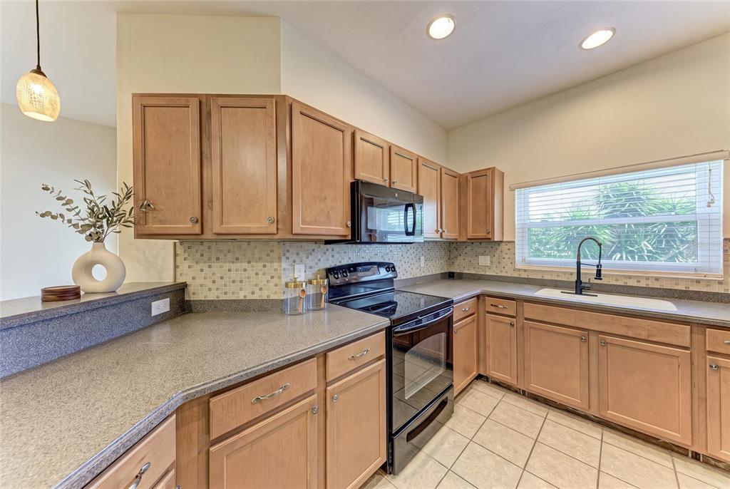 A kitchen features light wood cabinets, dark countertops, a black stove, and a tiled backsplash — 1510 GRANTHAM DRIVE, SARASOTA, FL