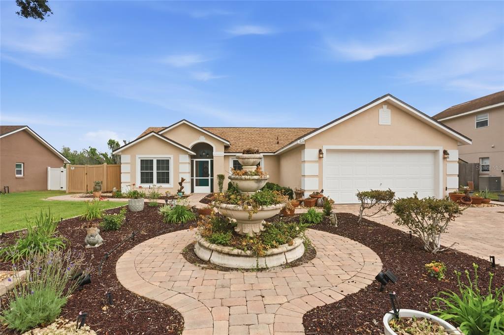 A single-story house with a tan exterior, a two-car garage, and a landscaped front yard — 204 GREENWICH STREET, DAVENPORT, FL