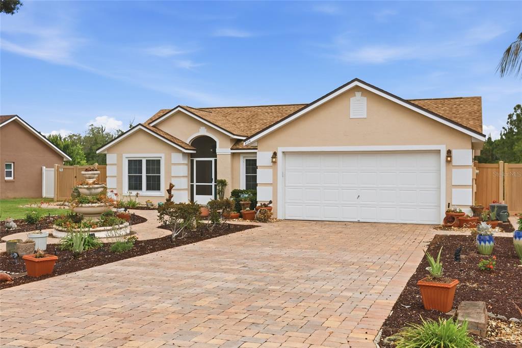 A tan single-story house features a paved walkway, a screened front door, and landscaped beds — 204 GREENWICH STREET, DAVENPORT, FL