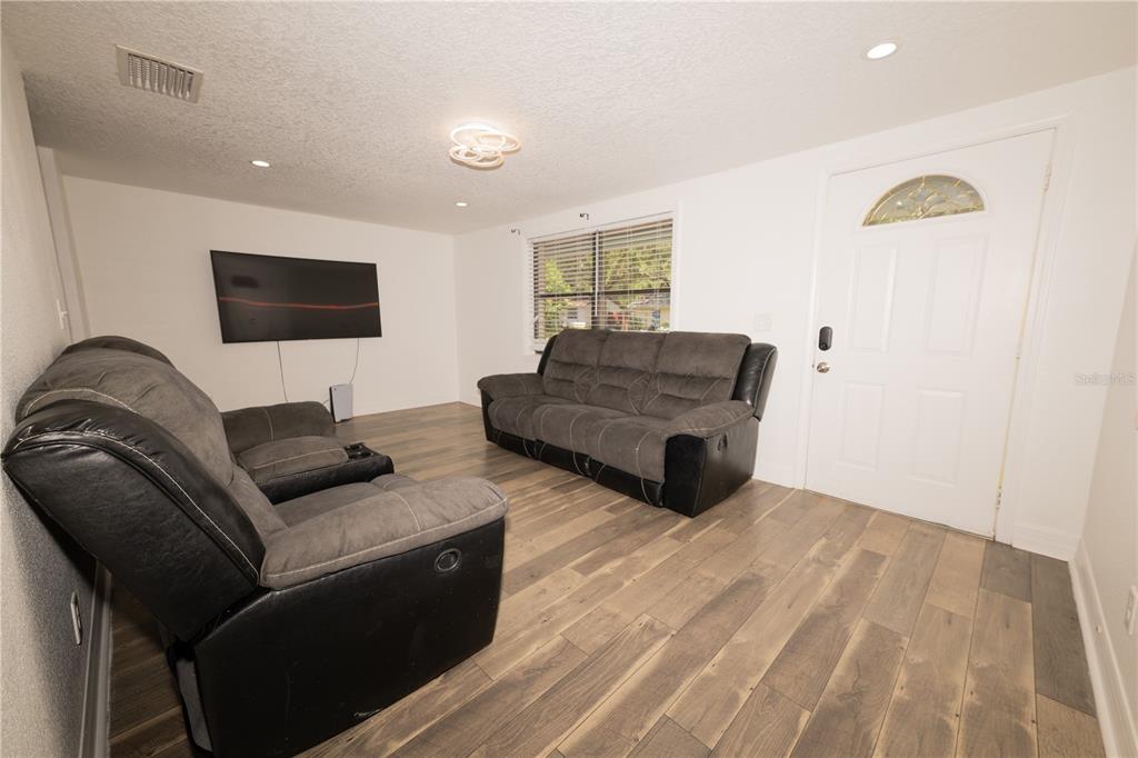A living room features gray wood-look flooring, two dark gray sofas, and a wall-mounted television — 39736 MEADOWOOD LOOP, ZEPHYRHILLS, FL
