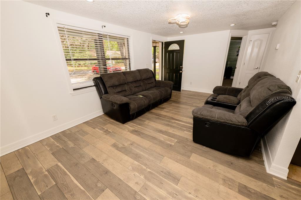 A living room features two dark gray sofas, wood-look flooring, and a black front door — 39736 MEADOWOOD LOOP, ZEPHYRHILLS, FL