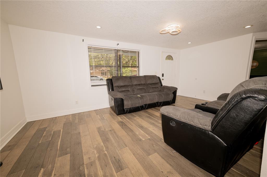 A living room with gray wood-look flooring, white walls, and two dark gray reclining sofas — 39736 MEADOWOOD LOOP, ZEPHYRHILLS, FL